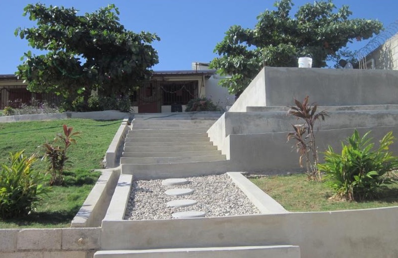 The Chez Moi house: concrete steps and a stone path lead up through a landscaped lawn to the house beneath two leafy trees