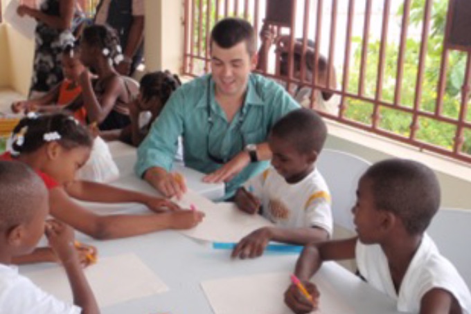 An instructor sits at a table with a group of young students, helping them with their written work